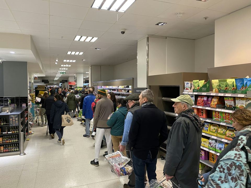 Shoppers with baskets lined up along a supermarket aisle waiting to check out